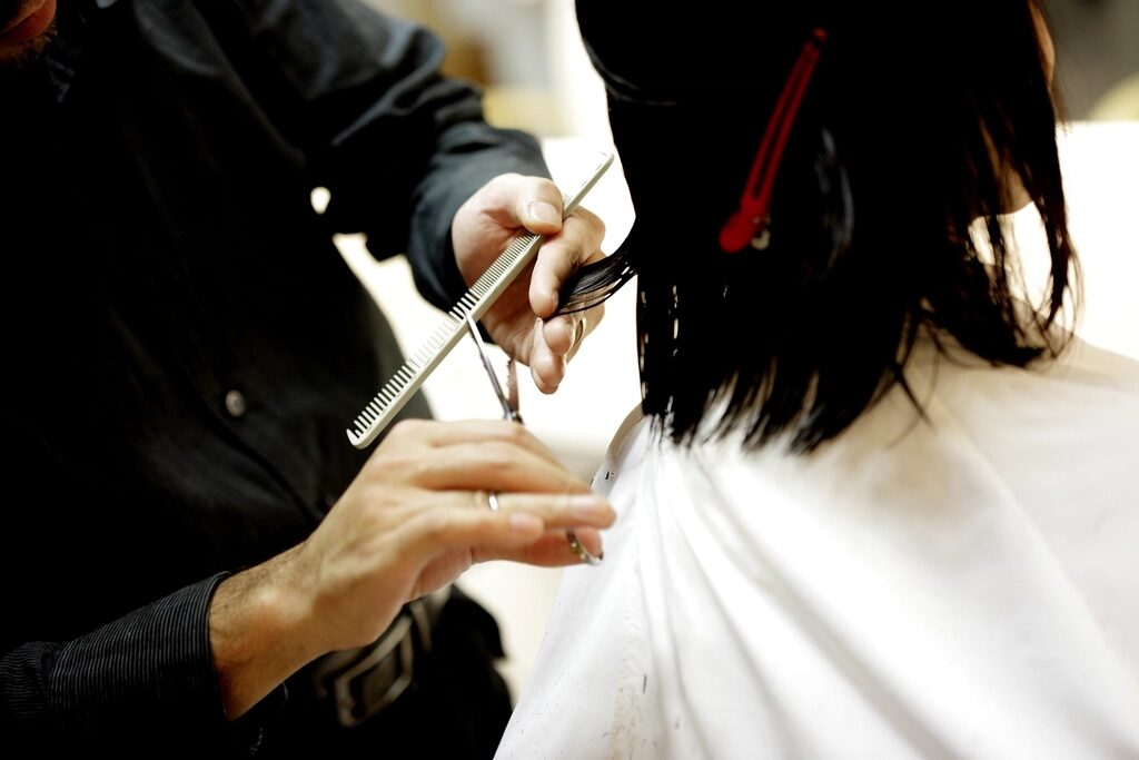 Stylist cutting a client's dark shoulder-length hair with scissors