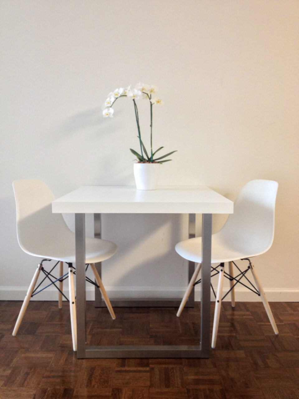 White dining table with an orchid and two chairs