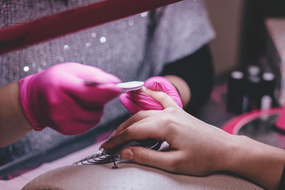 Nail technician in pink gloves filing a client's nails