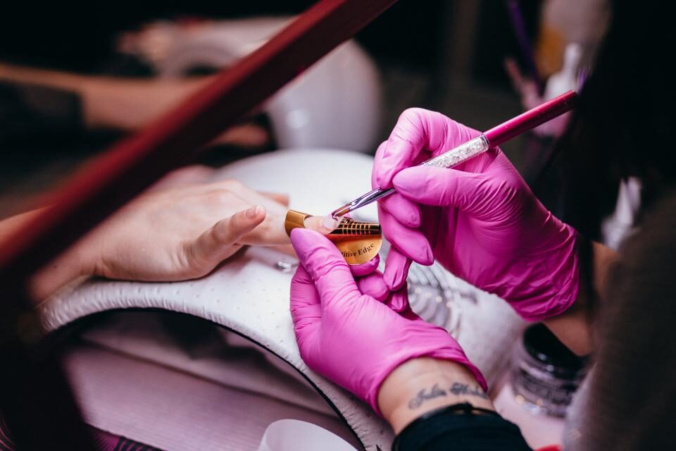 Nail technician in pink gloves painting a client's nails