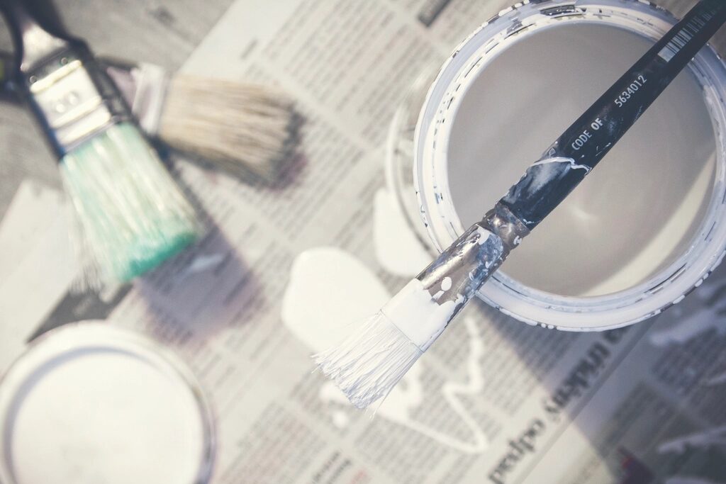Brushes and an open tin of white paint on newspaper