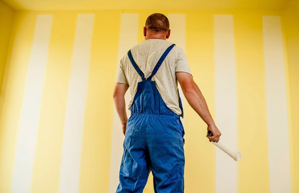 Painter in overalls facing a striped wall
