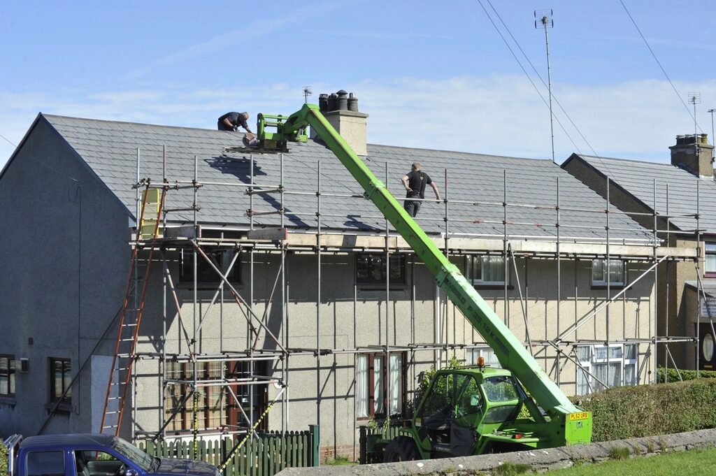 A roofing crew re-covering a house roof from scaffolding and a lift