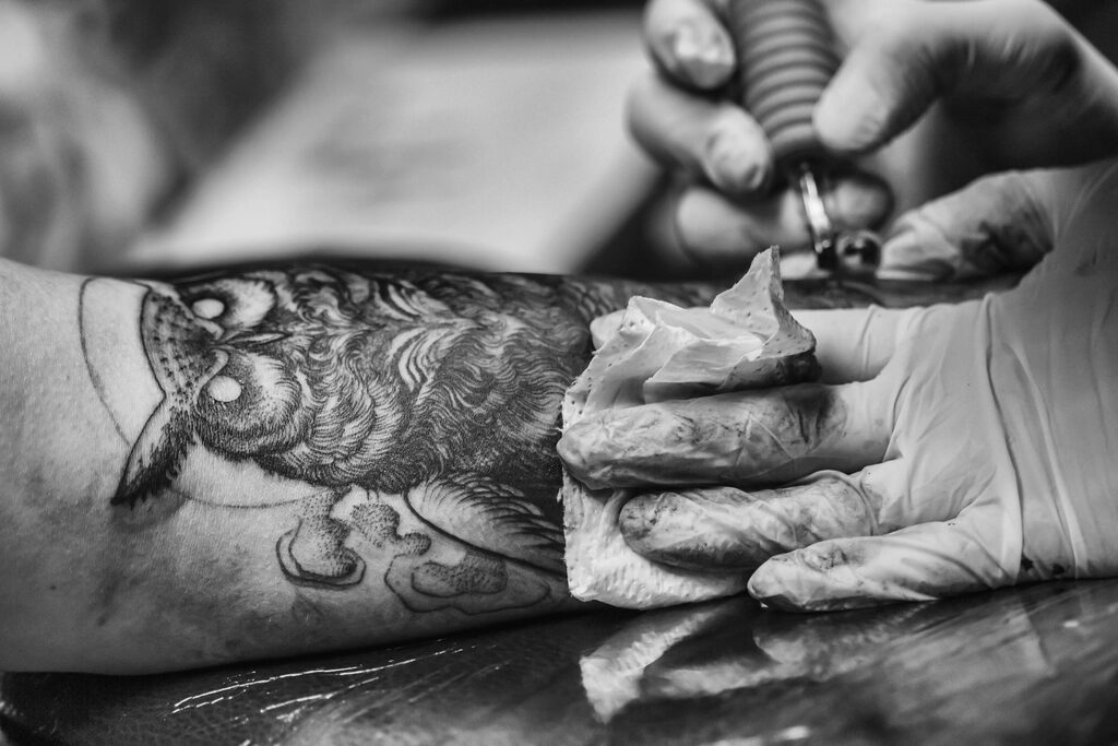 Black and grey owl tattoo on a forearm being wiped clean