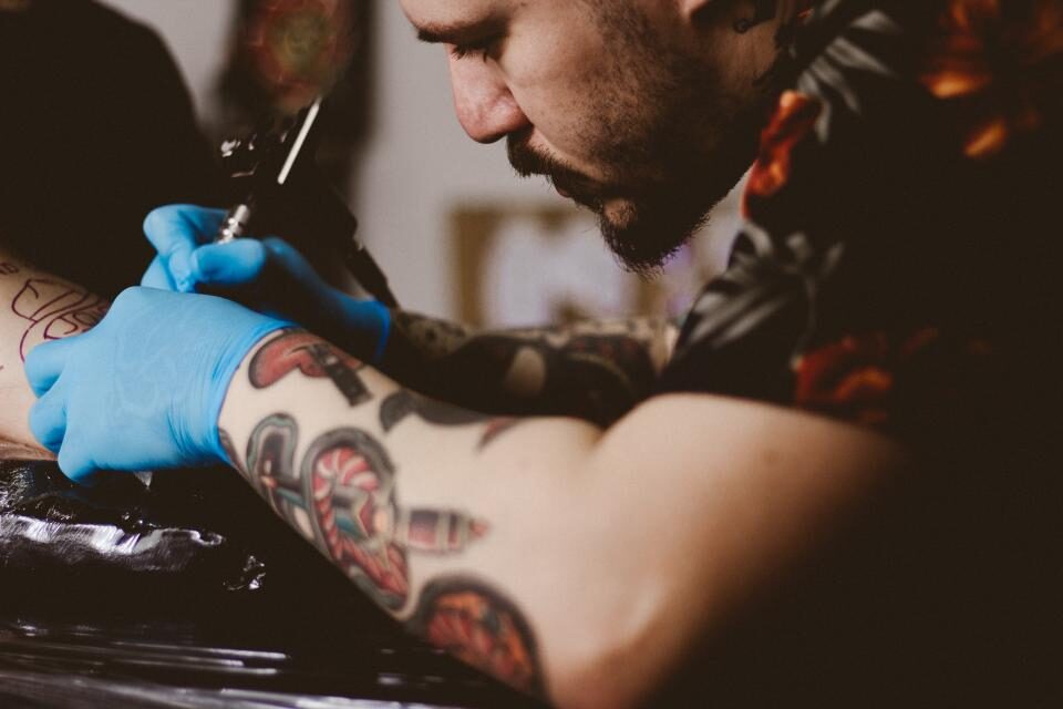 Tattoo artist in blue gloves working on a color piece on a client's forearm