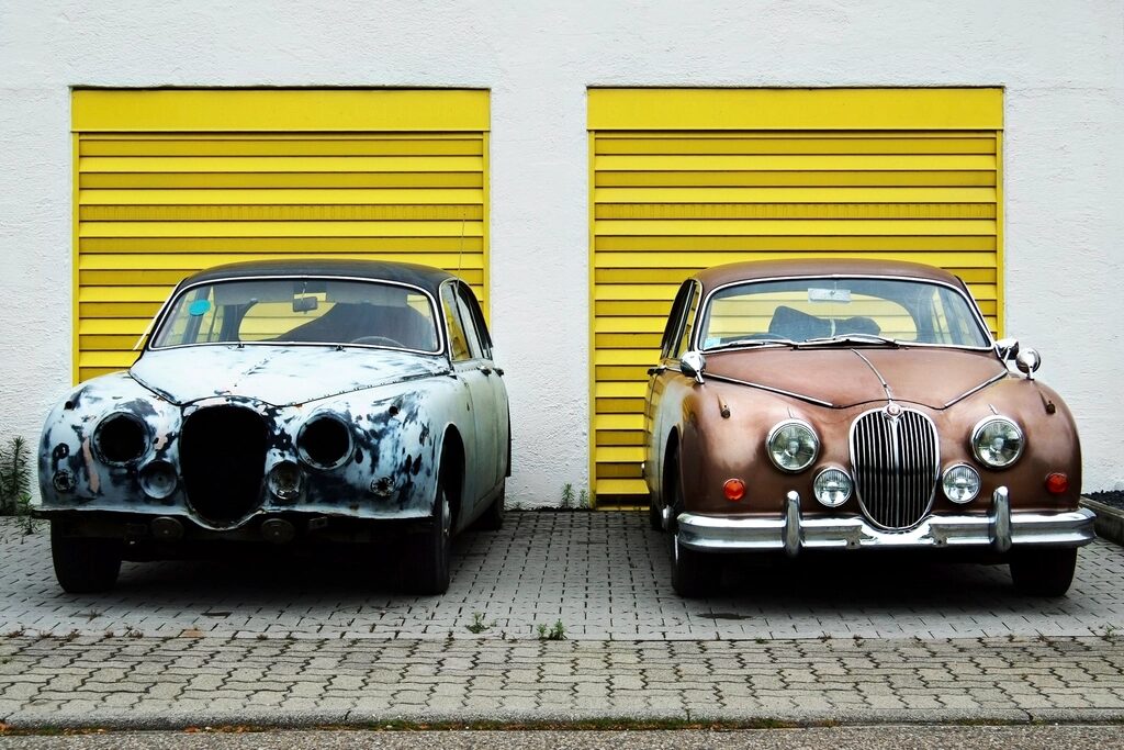 Two classic saloons parked outside yellow garage doors